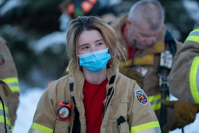 Firefighter wearing a mask and uniform, with a serious expression, amid snowy surroundings.